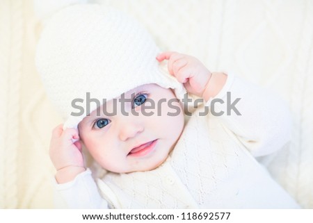 Little baby in a white knitted sweater and hat on a white cable knit blanket