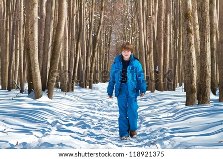 Cute boy walking in a snowy forest on a cold sunny day