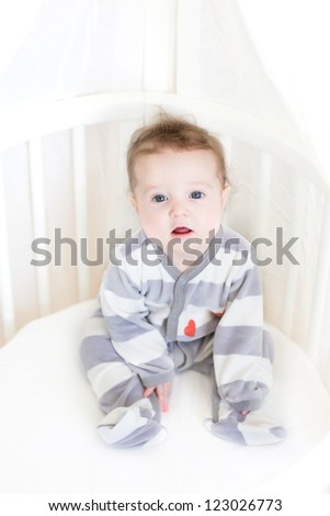 Sweet baby girl sitting in a white round crib