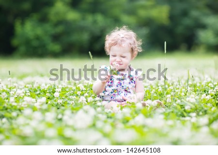 Funny curly baby girl smelling summer flowers