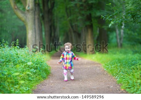 Cute baby girl in rubber rain boots walking in a rainy park