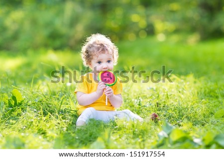 Cute curly baby girl eating water melon candy in a sunny park