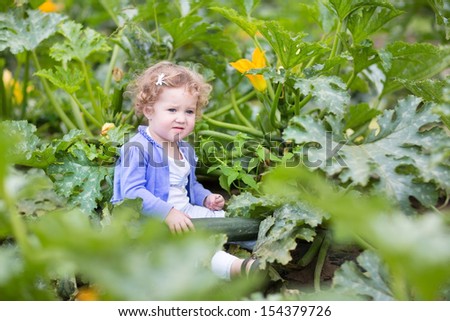 Funny cute baby girl playing on a farm in a zucchini field in autumn