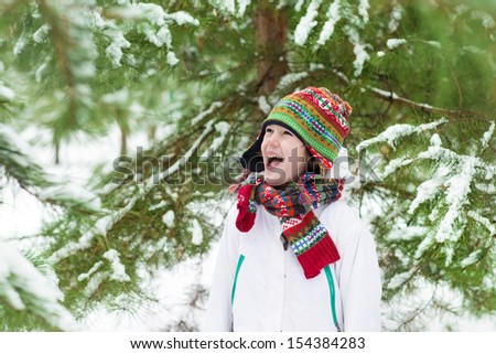Funny little boy screaming with joy playing snow ball fight in a snowy winter park under Christmas trees