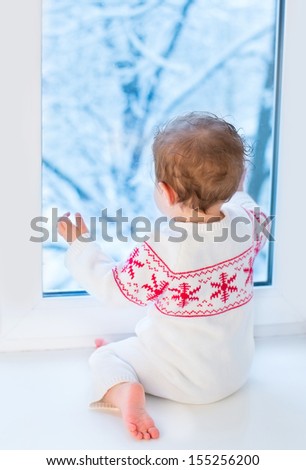 Little baby watching out of a window to a snowy garden on Christmas day