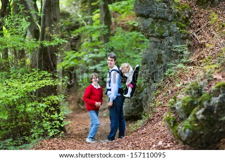 Young active father hiking in a beautiful autumn cliff and forest landscape with his school age son and baby daughter sitting in a back carrier