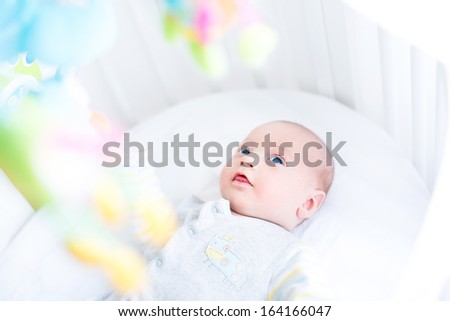 Cute newborn baby watching colorful toys in his white crib