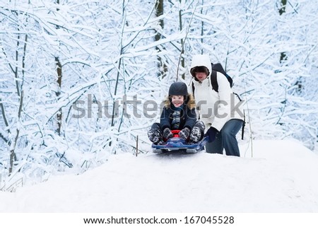 Young happy father and his cute laughing son sledding together in a snowy park