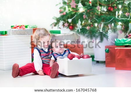 Little toddler girl and her newborn brother helping to decorate a Christmas tree