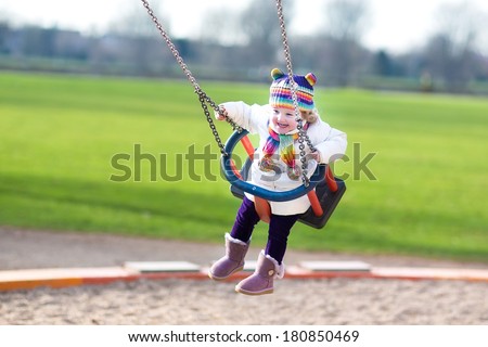 Happy laughing toddler girl swinging on a playground on a sunny spring day