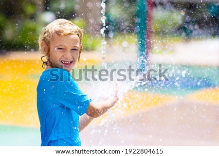 Child playing under tip bucket in water park. Kids play with splash dump bucket. Family fun in amusement center on hot summer day. Sun protection for children. Water slides for kid.