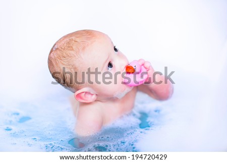Cute baby boy taking a bubble bath with foam playing in water with a rubber duck toy after shower