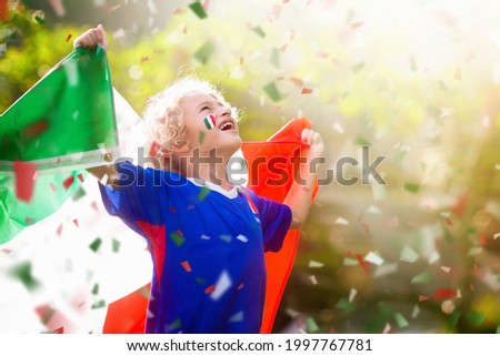 Italy football fan. Italian kids play soccer on outdoor field. Cheering team fans celebrate victory. Children score a goal at football game. Little boy in Italia jersey kicking ball on outdoor pitch.