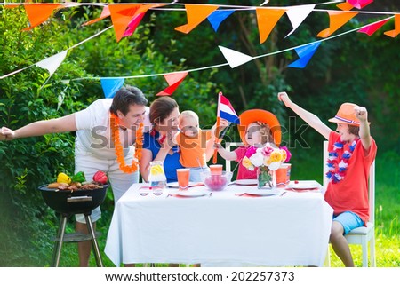 Happy big Dutch family with kids celebrating a national holiday or sport victory having fun at a grill party in a garden decorated with flags of Netherlands, screaming Hup Holland