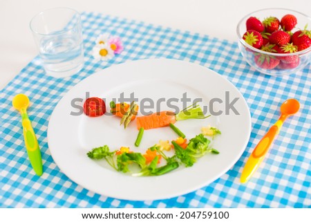 Healthy vegetarian lunch for little kids, vegetables and fruit served as animals, corn, broccoli, carrots and fresh strawberry helping children to learn eating right and clean