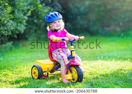 Cute funny toddler girl riding her bike wearing a safety helmet enjoying a nice sunny day in a summer garden playing outdoors
