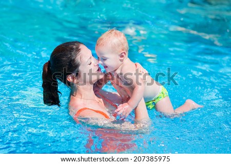 Happy young mother and her little son, adorable laughing baby boy having fun together in an outdoor swimming pool on a hot summer day during vacation in a tropical resort