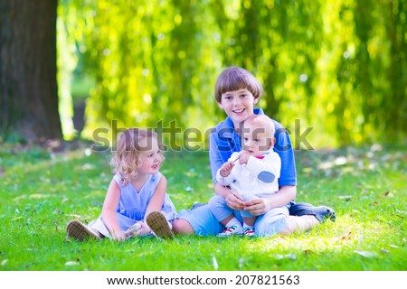 Three happy kids, brothers and sister, laughing teenager boy, little baby and a funny curly girl playing together with flowers in a sunny garden of their backyard  on a warm sunny day