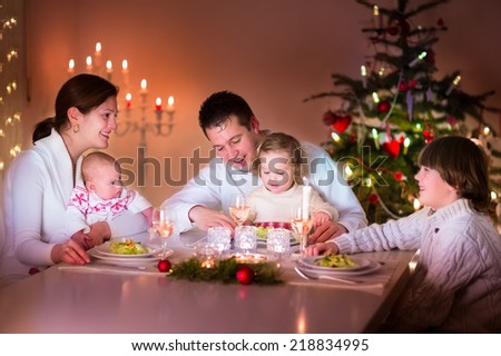 Big happy young family with three children enjoying Christmas dinner celebration, parents and kids - teen age boy, little toddler girl and baby in a dark dining room with candles and Xmas tree