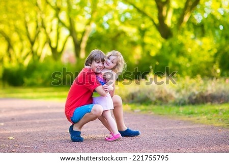 Happy children hugging and playing in a park, laughing boy and his funny curly toddler sister, adorable little girl having fun in a sunny autumn park