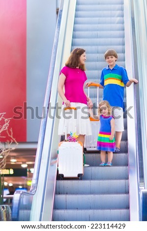 Young mother with two kids traveling by airplane at Dusseldorf International airport, standing at an escalator holding colorful luggage for summer beach vacation