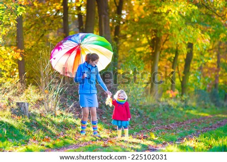 Happy young mother and her adorable toddler daughter, cute curly little girl in a colorful dress and warm coat, playing together in a beautiful autumn park enjoying a sunny fall day outdoors