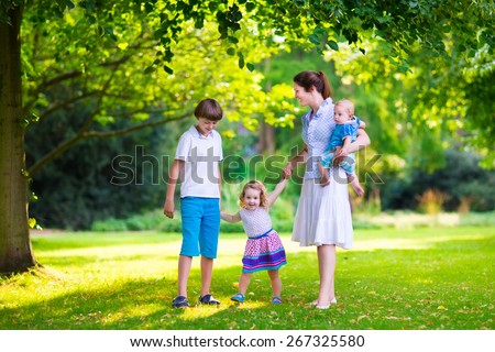 Happy family with three kids in a park. Young mother with children, little toddler girl, school age boy and baby playing in a sunny summer garden, walking and holding hands with her son and daughter.