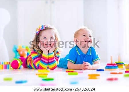 Kids playing with toys. Two children, cute toddler girl and funny baby boy, playing with wooden toy blocks, building towers at home or day care. Educational child toys for preschool and kindergarten.