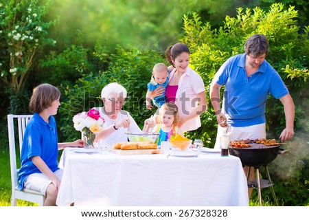 Grill barbecue backyard party. Happy big family, mother, father, age son, cute toddler daughter and baby, enjoying BBQ lunch with grandmother eating grilled meat in the garden with salad and bread.