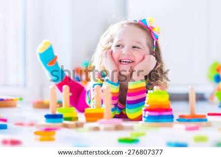 Child playing with wooden toys at preschool. Cute toddler girl having fun with toy blocks, building a tower at home or day care. Educational kids toy for nursery or kindergarten.