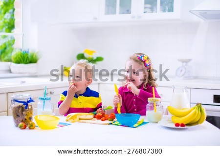 Little girl and boy preparing breakfast in kitchen. Healthy food for children. Child drinking milk and eating fruit. Happy preschooler enjoying morning meal, cereal, banana, strawberry. Kids cooking