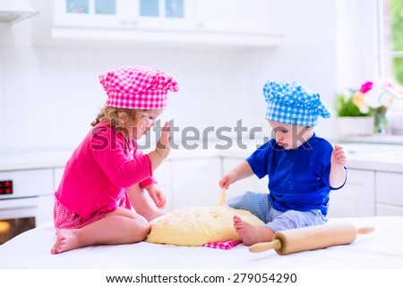 Kids baking. Two children cooking. Little girl and baby boy cook and bake in a white kitchen with modern oven. Brother and sister in chef hats making a pie for dinner.