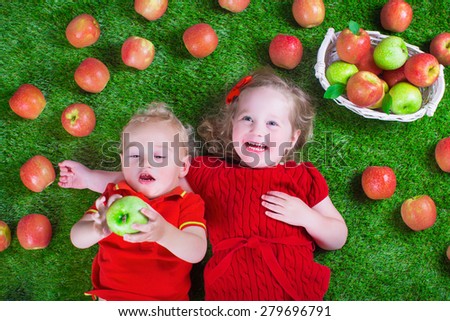 Child eating apple. Little girl and baby boy play peek a boo holding fresh ripe apples. Kids eat snack relaxing on a lawn. Children summer fun on a farm picking healthy fruit.