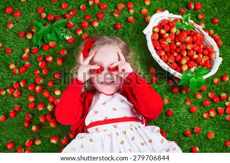 Child eating strawberry. Little girl playing peek a boo holding fresh ripe strawberries. Kids eating fruit relaxing on a lawn. Children summer fun on a farm picking berry.