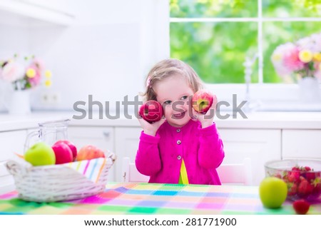 Child eating breakfast. Kids eat in a white kitchen. Children having fresh fruit. Little kid playing peek a boo with apples. Preschooler girl with apple and strawberry. Healthy nutrition for toddlers.
