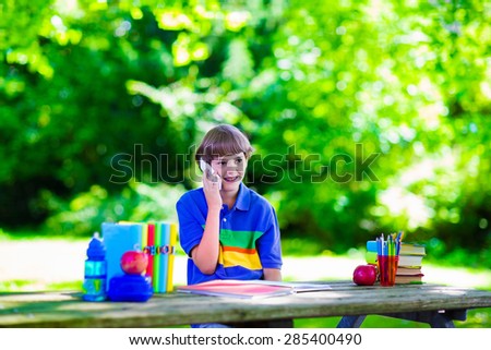 Child in school with telephone. Smart teenager boy studying and learning outdoors, reading books. Children calling, texting with smartphone. Kids talking on the phone. Students with modern gadgets.