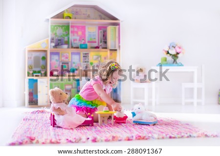 Little girl playing. Kids with doll house and stuffed animal toys. Children sit on a pink rug in a play room at home or kindergarten. Toddler kid with plush toy and dolls. Birthday party for child.