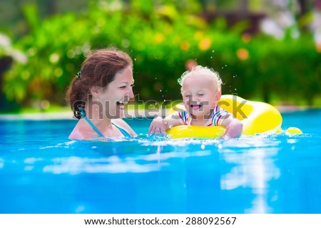 Mother and baby in swimming pool. Parent and child swim in a tropical resort. Summer outdoor activity for family with kids. Vacation and traveling with young children. Inflatable toys for water fun.