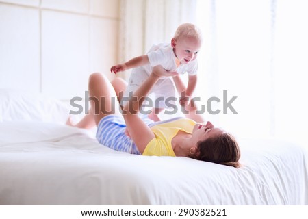 Mother and baby in bed. Young mom playing with her newborn son. Child and parent together at home. Family with kids in the morning. Woman relaxing with kid in a sunny bedroom. Happiness and motherhood