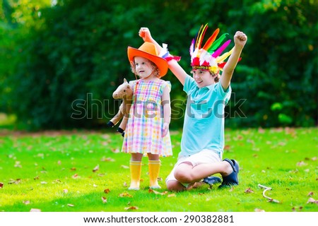 Kids in cowboy and cowgirl costumes playing outdoors. Children play with toy horse. Boy in Native American hat on Thanksgiving party. Toddler kid and school child during trick or treat at Halloween.
