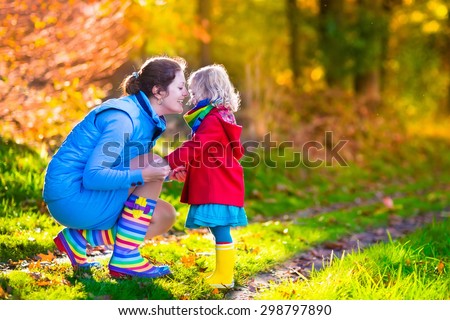 Mother and daughter play in autumn park. Parent and child walk in the forest on a sunny fall day. Children playing outdoors with yellow maple leaf. Toddler girl picking golden leaves. Mom hugging kid.