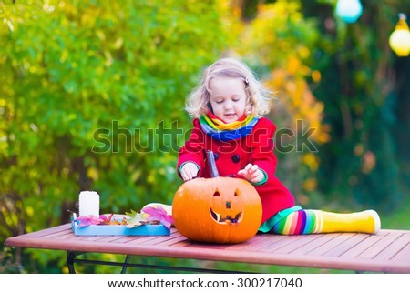 Little girl carving pumpkin at Halloween. Dressed up child trick or treating. Kids trick or treat. Child in witch costume playing in autumn park. Toddler kid with jack-o-lantern.