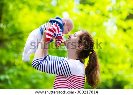 Mother holding newborn baby in a park. Mom playing with her new born son in the garden. Family with kids play outdoors. Young woman hugging little boy. Parents and children having fun in summer.