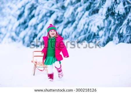 Little girl enjoying a sleigh ride. Child sledding. Toddler kid riding a sledge. Children play outdoors in snow. Kids sled in the Alps mountains in winter. Outdoor fun for family Christmas vacation.