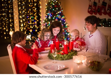 Big family with three children celebrating Christmas at home. Festive dinner at fireplace and Xmas tree. Parent and kids eating at fire place in decorated room. Child lighting advent wreath candle.