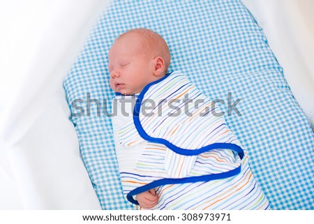 Adorable newborn baby sleeping swaddled in white bed. New born boy taking a nap in blue crib. Kids sleep. Swaddling for infants. Little kid wrapped in warm blanket relaxing in crib with canopy.