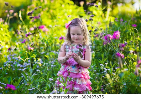 Little girl playing with flowers in the garden. Kids play outdoors in summer. Children gardening. Child planting flower in the backyard. Gardener at work. Kid working with plants.