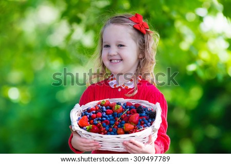 Child picking berries on a farm. Little girl eating strawberry, raspberry, blueberry, blackberry, red and black currant. Kids eat berry. Healthy nutrition for children. Toddler kid with fruit basket.