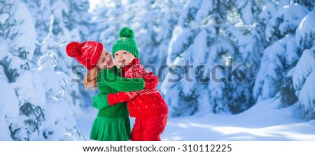 Little girl and boy in red and green knitted hat catching snowflakes in winter park on Christmas eve. Kids play outdoor in snowy winter forest. Children catch snow flake on Xmas. Large panorama banner