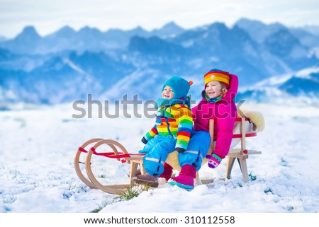 Little girl and baby boy enjoying a sleigh ride in the Alps mountains. Child sledding. Toddler kid riding a sledge. Children play outdoors in snow. Kids sled. Outdoor winter fun for Christmas vacation